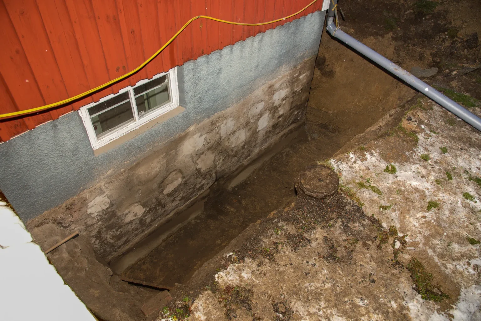 Uppgrävt runt rött hus för dränering.